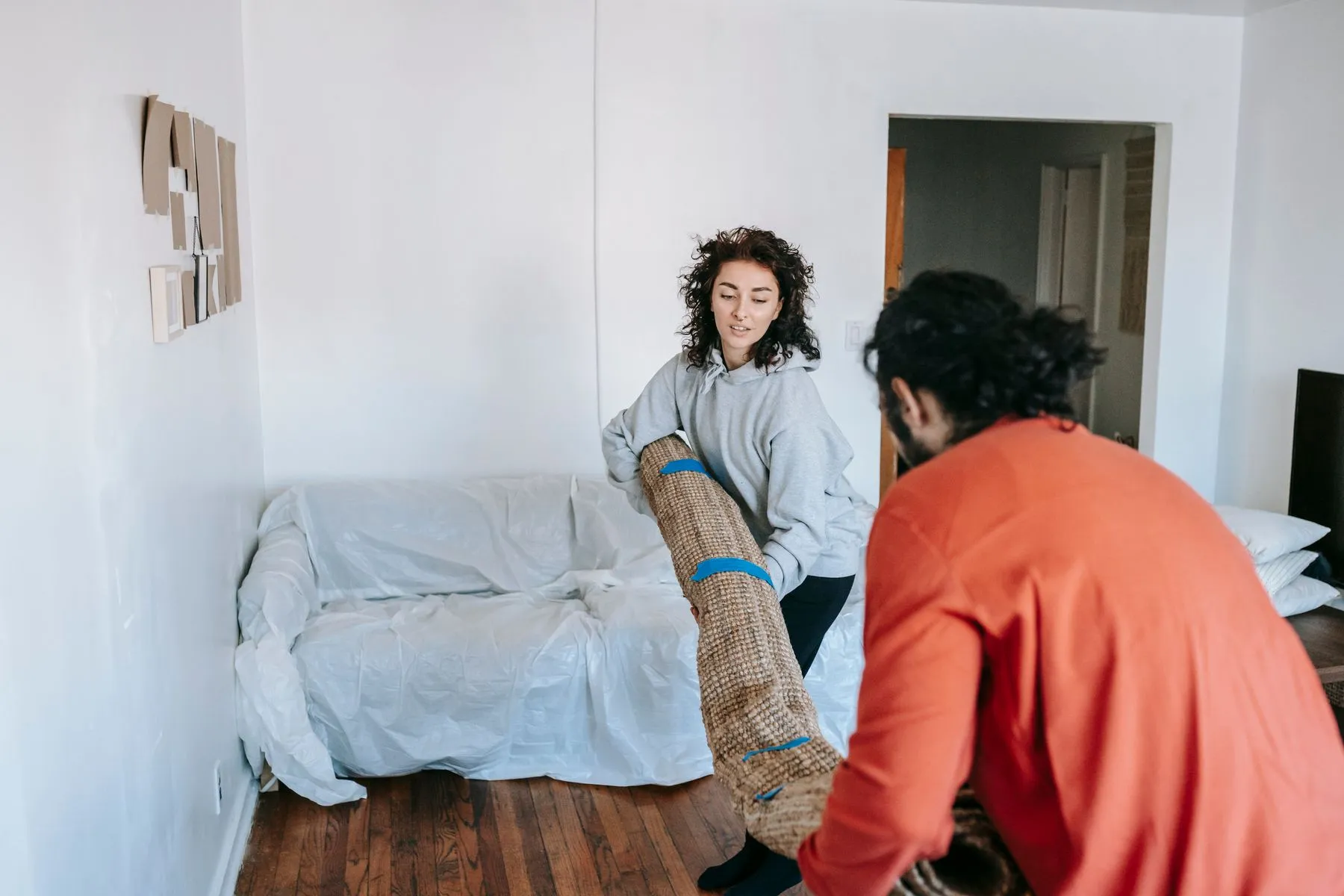 Two people lifting a rolled rug in a residential room
